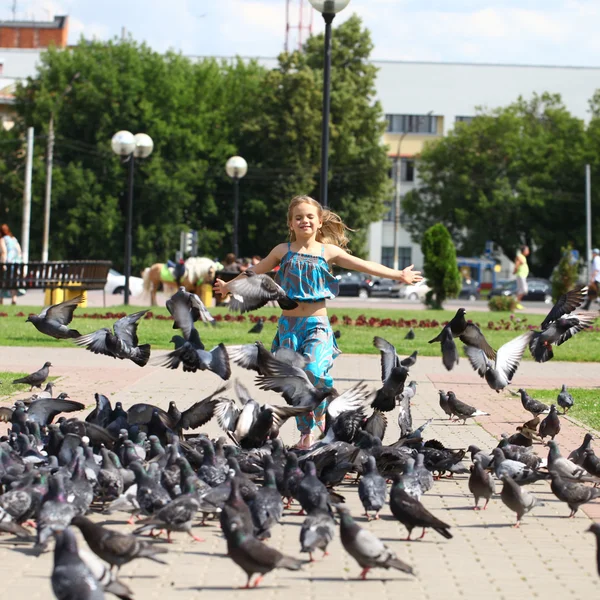 Glad flicka går genom en flock duvor på torget — Stockfoto