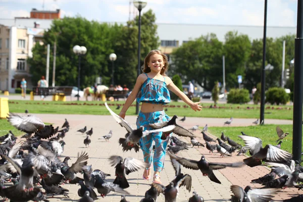 Joven chica feliz corre a través de un rebaño de palomas en la plaza —  Fotos de Stock