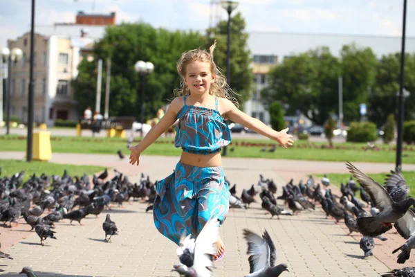 Young happy girl runs through a flock of pigeons on the square — Stock Photo, Image