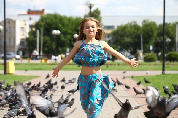 Joven chica feliz corre a través de un rebaño de palomas en la plaza —  Fotos de Stock