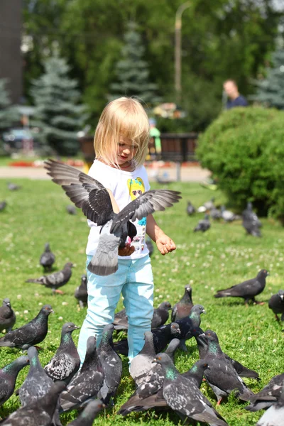 Счастливая маленькая девочка кормит голубей на городской улице — стоковое фото