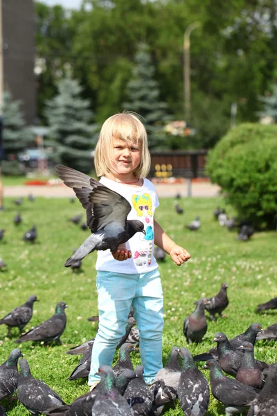 Lycklig liten flicka som matar duvor i staden gatan — Stockfoto