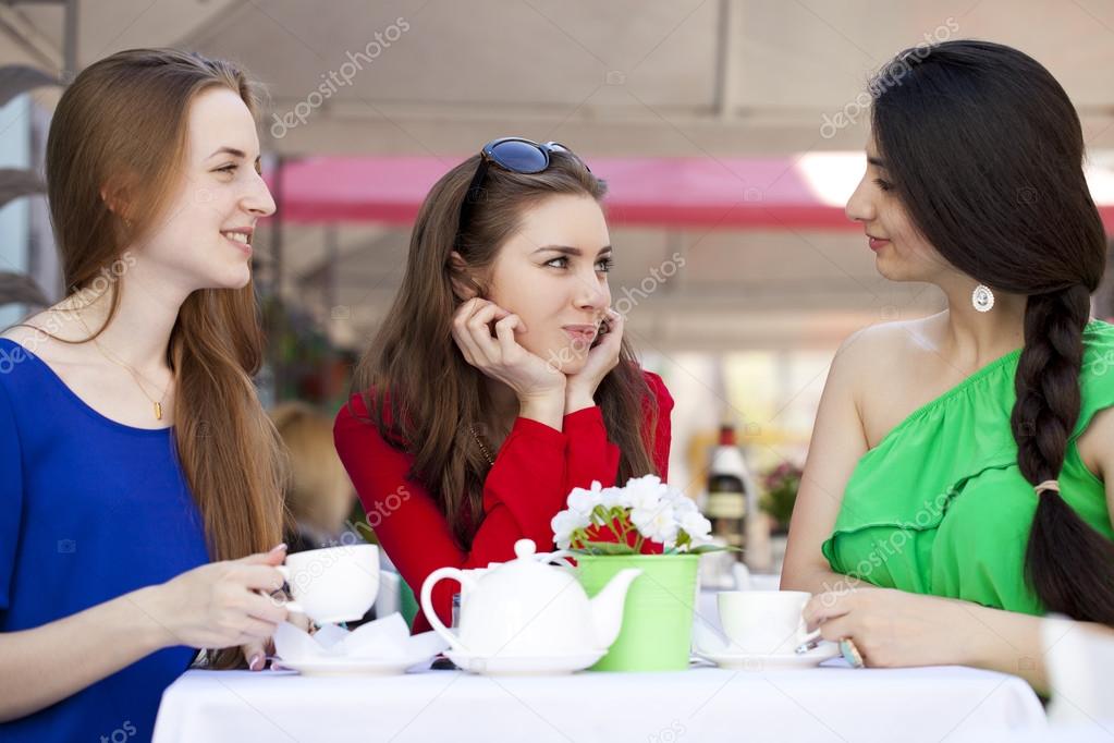 Three happy girlfriends woman sitting at a table in the summer c