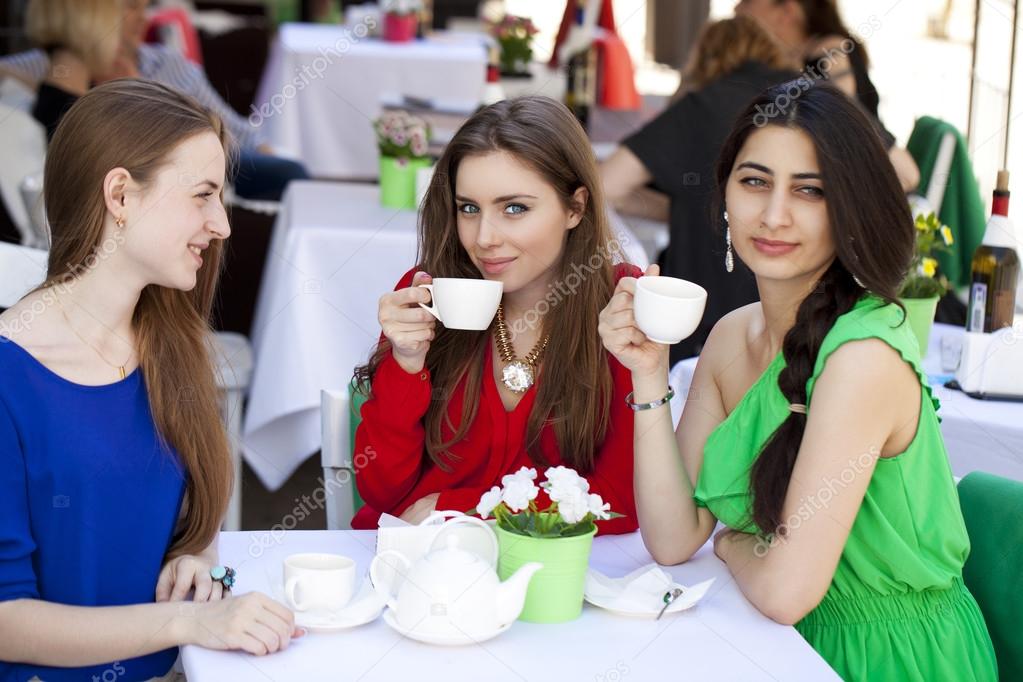 Three happy girlfriends woman sitting at a table in the summer c