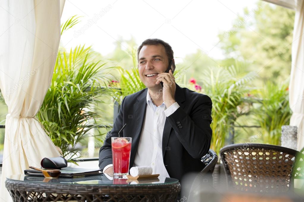 Businessman talking on a cell phone and drinking a cocktail 