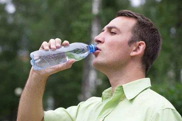 Un bel homme qui boit de l'eau dans un parc — Photo