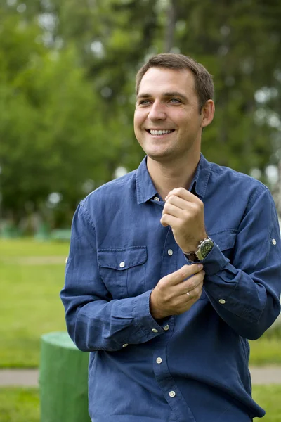 Jovem homem bonito em uma camisa azul no fundo do verão p — Fotografia de Stock