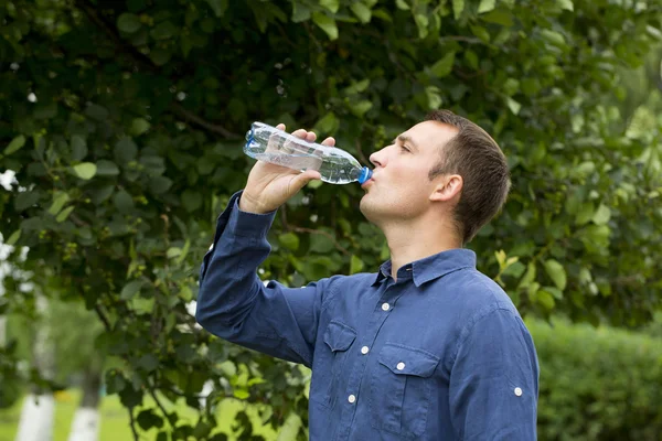 Schöner Mann, der Wasser in einem Park trinkt — Stockfoto