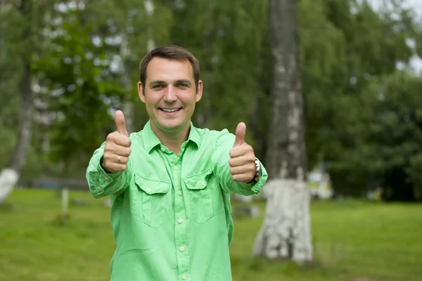 Joven hombre guapo con el pulgar arriba en una camisa verde en el backgro — Foto de Stock