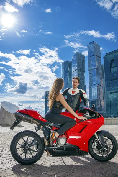 A guy and a young girl sit on a motorcycle on the background of skyscrapers and blue sky