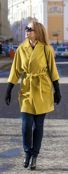 Jonge gelukkig blonde vrouw in gele jas wandelingen op lente straat — Stockfoto