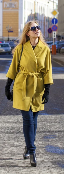 Jeune femme blonde heureuse en manteau jaune marche sur la rue du printemps — Photo