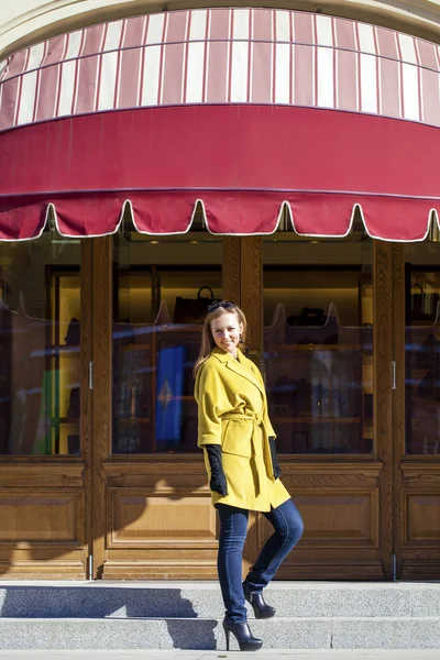Mladá šťastné blond žena ve žlutém kabátě chodí na jaře ulice — Stock fotografie