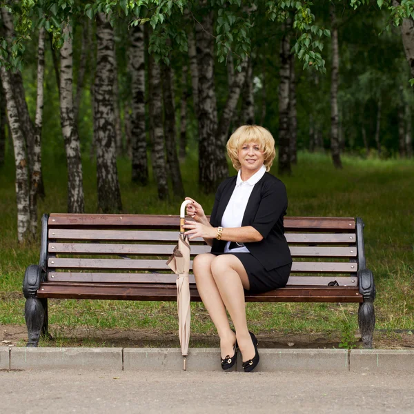 Äldre affärskvinna i jacka sittin på bänk — Stockfoto