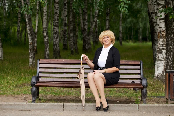 Äldre affärskvinna i jacka sittin på bänk — Stockfoto