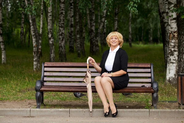 Äldre affärskvinna i jacka sittin på bänk — Stockfoto