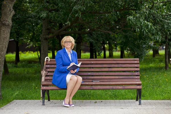 Yaşlı iş kadını ile günlük günlüğü bankta sittin ceketli — Stok fotoğraf