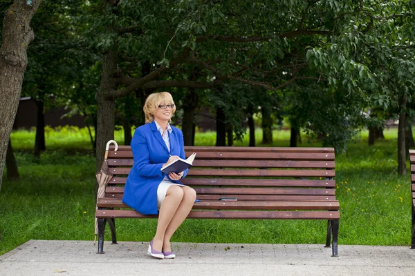 Reife Geschäftsfrau in Jacke mit Tagebuch auf einer Bank sitzend — Stockfoto