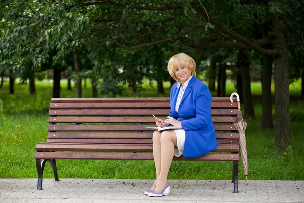 Пожилая деловая женщина в пиджаке сидит на скамейке с ежедневным журналом — стоковое фото