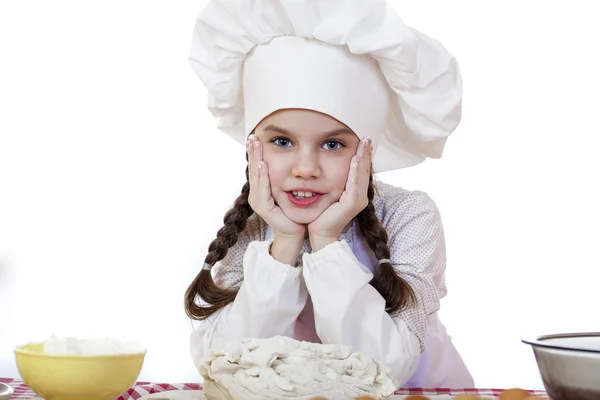 Little girl in a white apron and chefs hat knead the dough in th — Stock Photo, Image