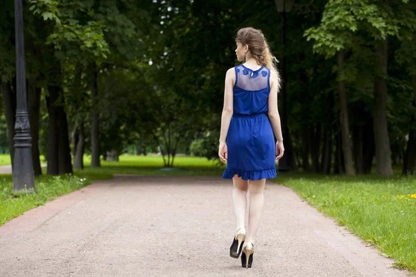 Schöne blonde Mädchen in blauem Kleid sitzt auf einer Bank im Sommer — Stockfoto