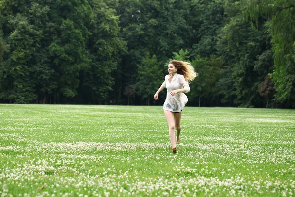 Молодая красивая девушка в белой рубашке бежит по зеленой — стоковое фото