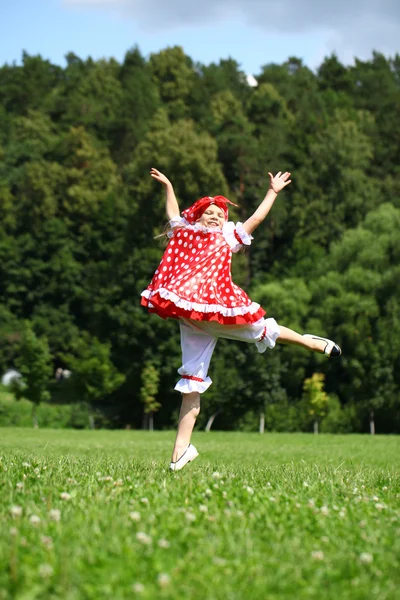 Kırmızı bir sundress çimlere sevinç için atlama, küçük kız — Stok fotoğraf