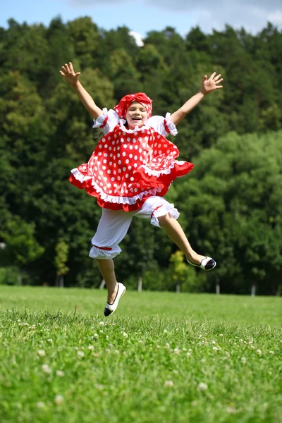 Menina em um vestido vermelho saltando de alegria no gramado — Fotografia de Stock