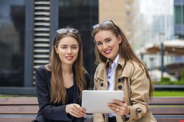 Zwei junge schöne Geschäftsfrauen sitzen auf einer Bank — Stockfoto