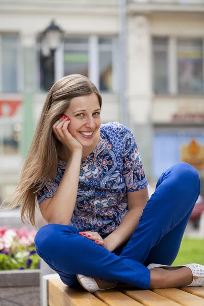 Gelukkig mooie jonge vrouw zit op een bankje — Stockfoto