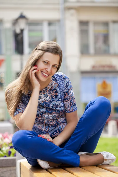 Glückliche schöne junge Frau sitzt auf einer Bank — Stockfoto