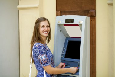 Young woman in summer dress using an automated teller machine  clipart
