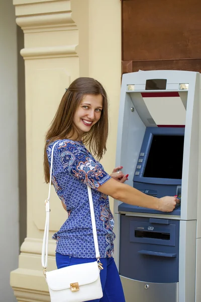 Mujer joven sonriente en una blusa azul retirando dinero del cajero automático —  Fotos de Stock