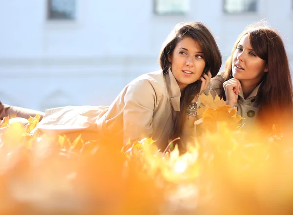 Sonrientes mujeres jóvenes atractivas con hojas de arce de otoño en el parque —  Fotos de Stock