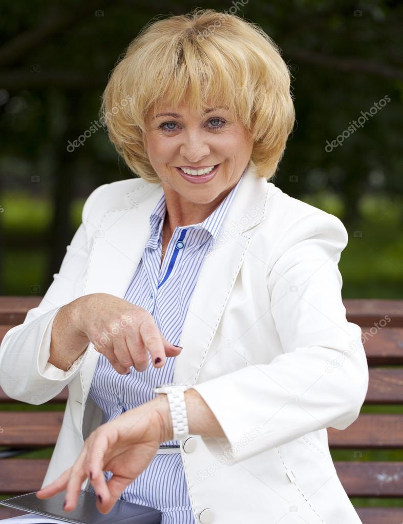 Mature business woman in a white jacket shows on his watch