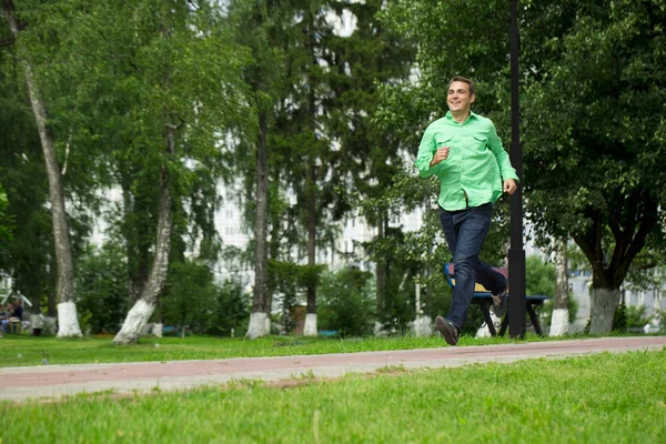 Young man in a green shirt and blue jeans running on summer park — Stockfoto