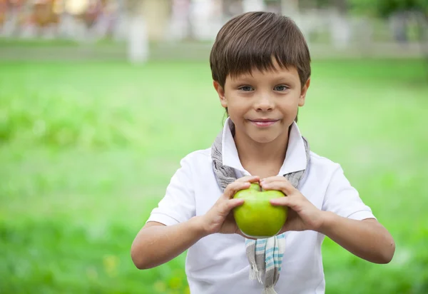 Malý chlapec drží zelené jablko na pozadí letní park — Stock fotografie