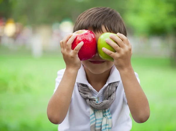 Malý chlapec drží dvě jablka na pozadí letní park — Stock fotografie