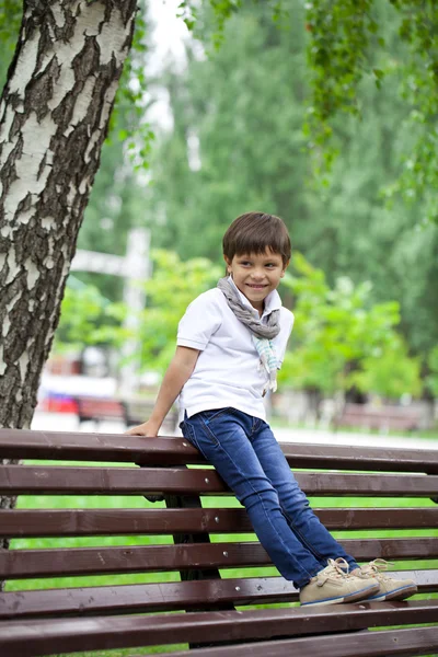 Menino sentado em um banco em um parque de verão — Fotografia de Stock