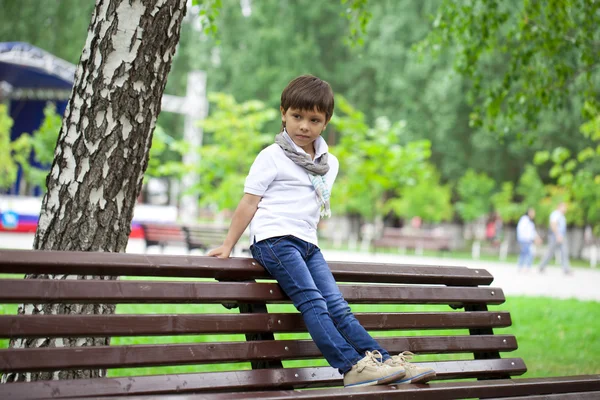 Маленький хлопчик сидить на лавці в літньому парку — стокове фото