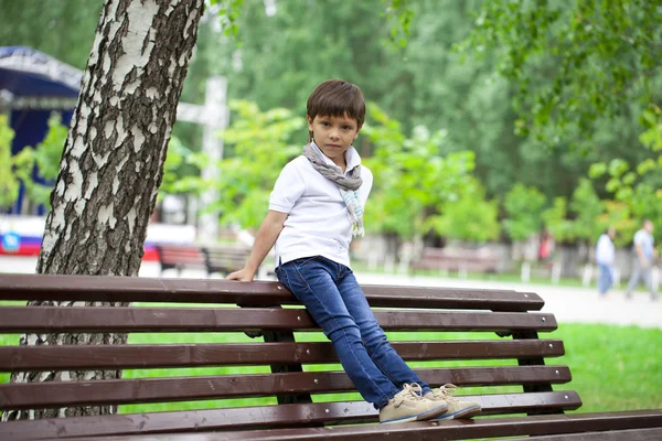 Petit garçon assis sur un banc dans un parc d'été — Photo