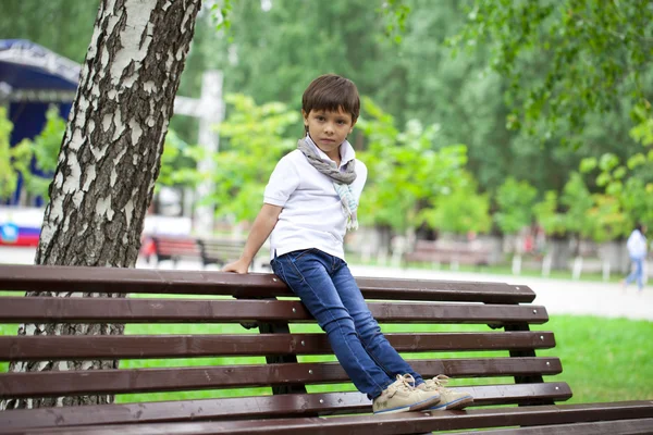 Liten pojke satt på en bänk i en sommar park — Stockfoto