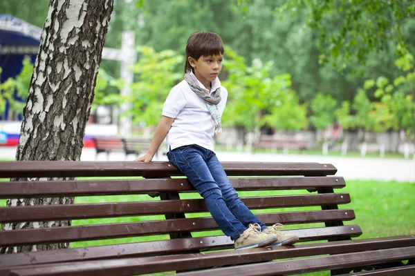 Petit garçon assis sur un banc dans un parc d'été — Photo