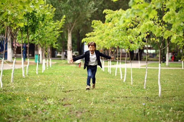 Happy little brunette boy runs in a summer park — Stock Photo, Image