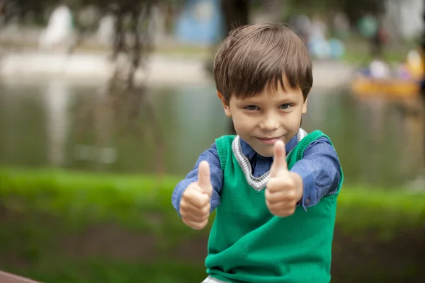 Хлопчик з великими пальцями вгору на фоні літнього парку — стокове фото