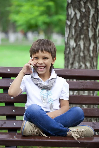 ベンチで携帯電話を呼び出す小さな男の子が座っています。 — ストック写真