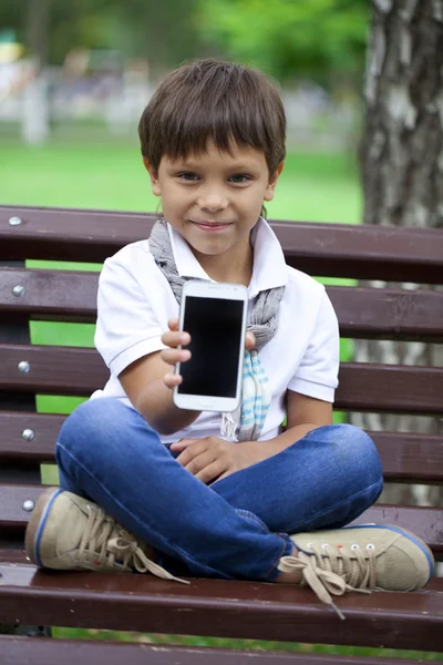 A little boy sits on a bench and showing mobile phone screen — Stock Photo, Image