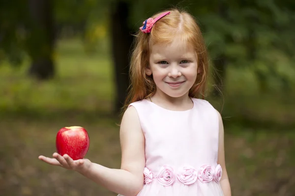 Menina ruiva segurando uma maçã vermelha em um fundo de gr — Fotografia de Stock