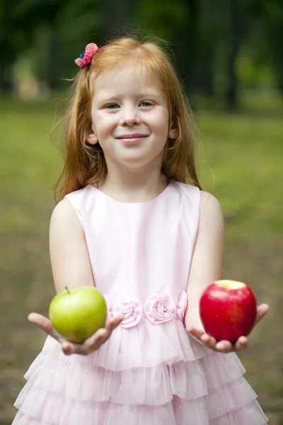 Little red-haired girl in a pink dress holding two apples