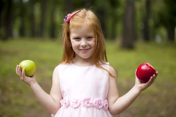 Little red-haired girl in a pink dress holding two apples — Stock Photo, Image